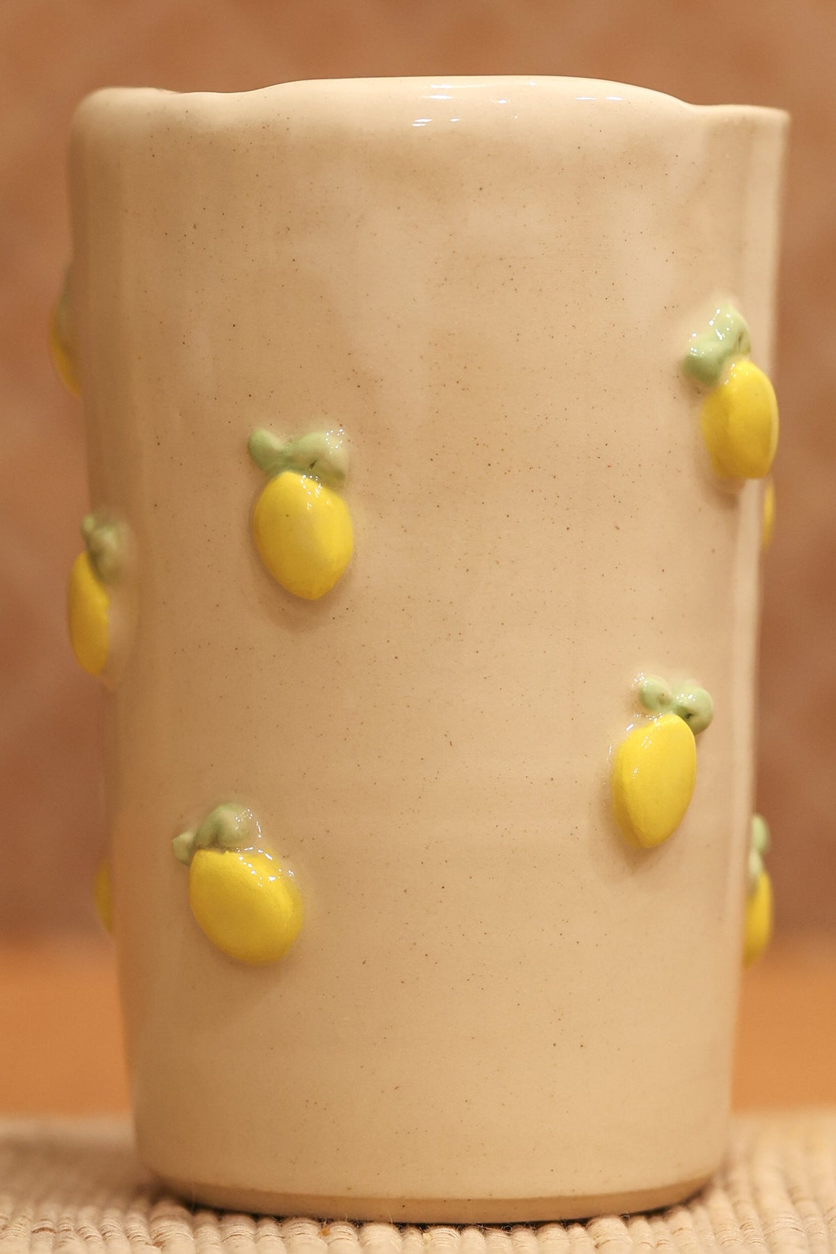 A handmade beige ceramic cup decorated with small yellow lemon shapes.